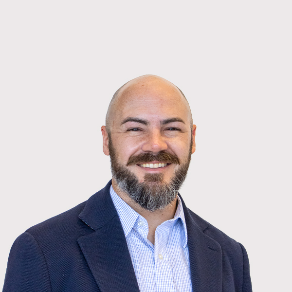 Professional headshot of a smiling man with a beard, wearing a blazer over a collared shirt.